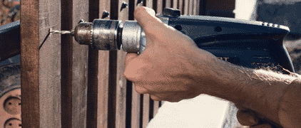 Man Hand Drilling Wooden Fence — H&D Building Supplies in Heatherbrae, NSW